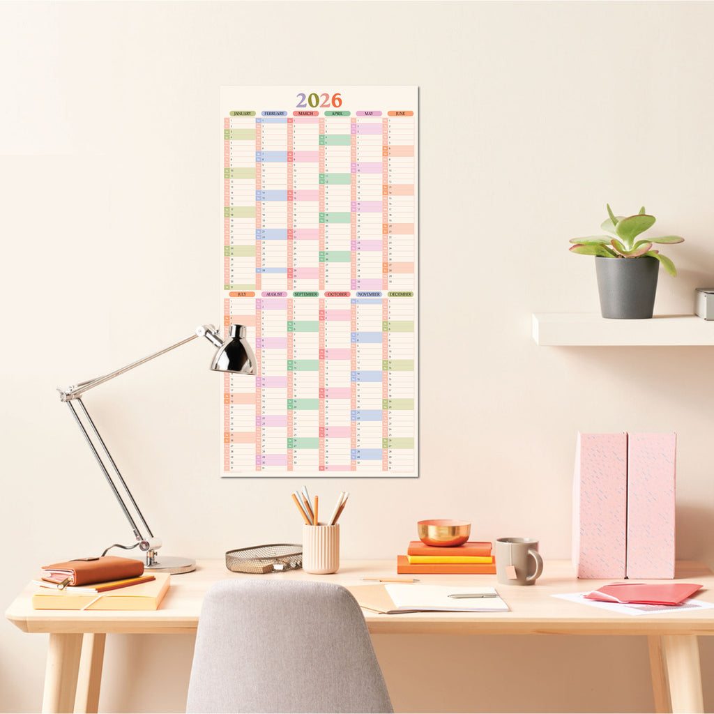 A vertical 2026 pastel compact wall planner hanging on a light-colored wall above a wooden desk.