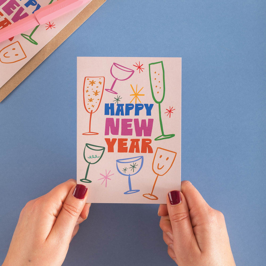 Hand holding a 'Happy New Year' card with colorful drink illustrations on a blue background