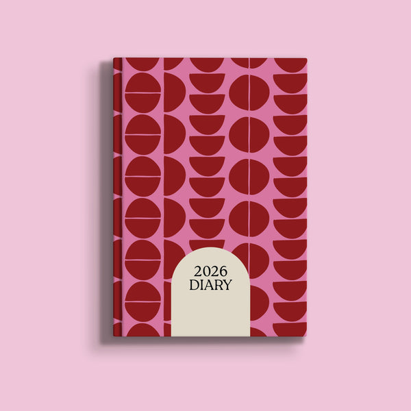 A pink A5 diary cover for 2026, featuring a geometric pattern of dark red circles and half-circles. A large, light beige arch-shaped section at the bottom center of the cover displays the text "2026 DIARY" in dark red.