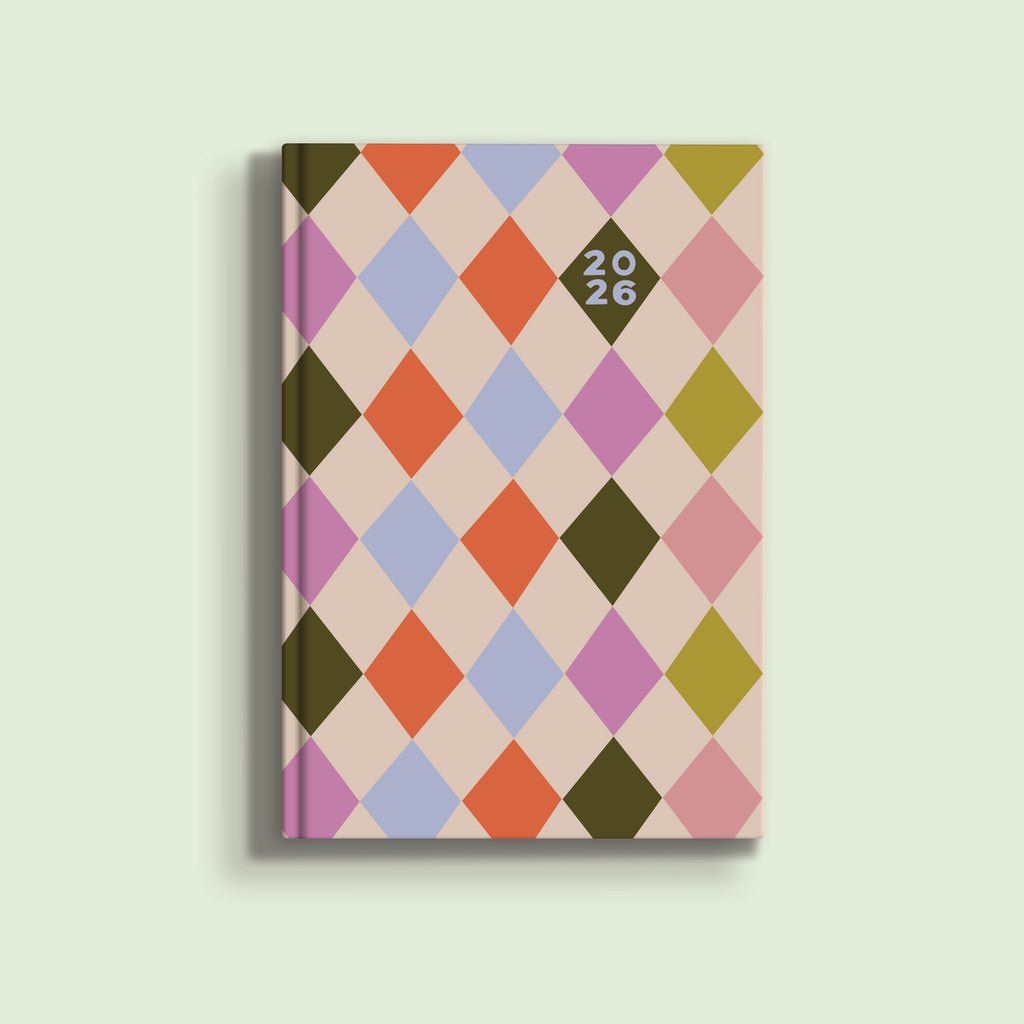 A light pink A5 diary cover for 2026, featuring a harlequin diamond pattern in various colors including dark green, orange, light blue, and purple. The year "2026" is written in black numbers inside a diamond shape near the top right.
