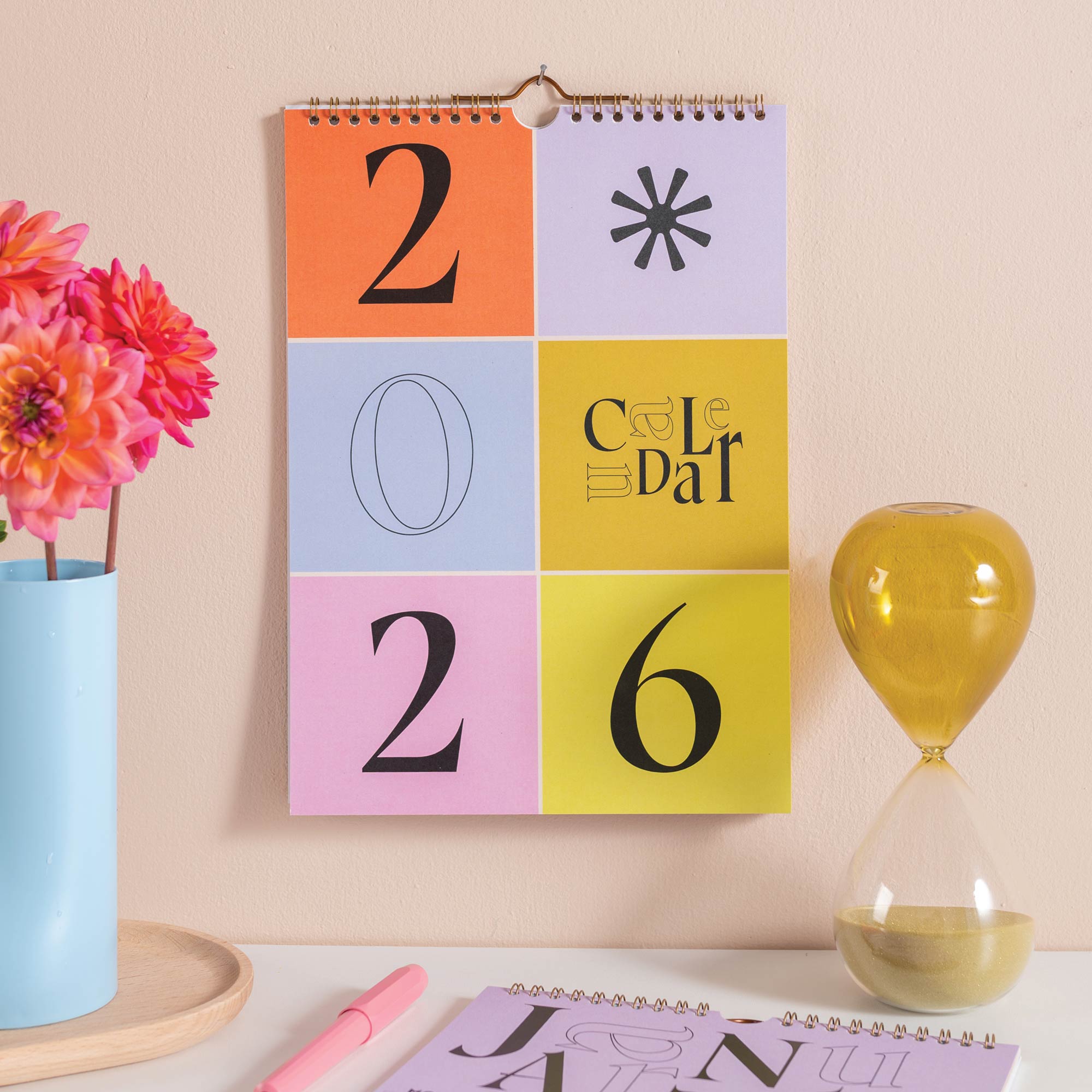 Good Tuesday's Colorful calendar with '2026' on a desk with flowers and an hourglass. 100% recycled paper. Bcorp Certified. 