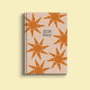 A light beige A5 diary cover for 2026, adorned with multiple stylized orange suns with wavy rays. The text "2026 diary" is centrally placed in dark blue, handwritten-style font.
