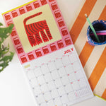 2026 bright and colourful Calendar with a Cat artwork by the artist Ashley Percival. Each month has a gird layout showing the days of the month and a colourful illustration from the artist.