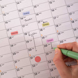 Hand holding a green pen over Good Tuesday's Black and White 2026 calendar with events marked. 100% recycled Paper, Made in the UK.