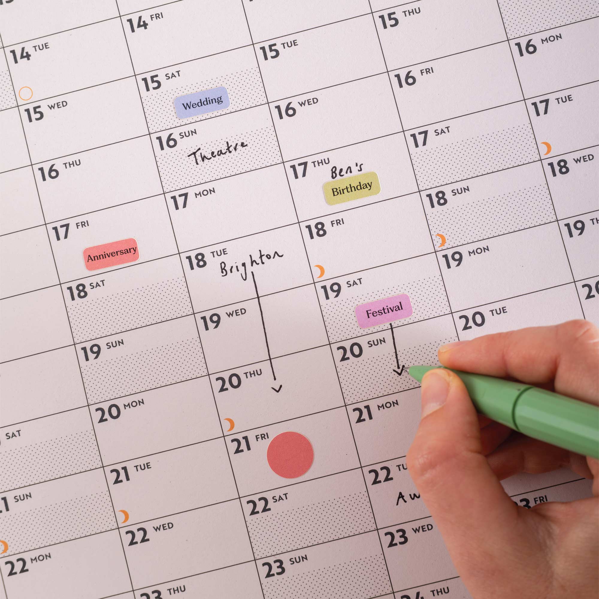 Hand holding a green pen over Good Tuesday's Black and White 2026 calendar with events marked. 100% recycled Paper, Made in the UK.