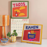 2027 wall calendar with colourful illustrated design by Abbie Franks hanging on wall