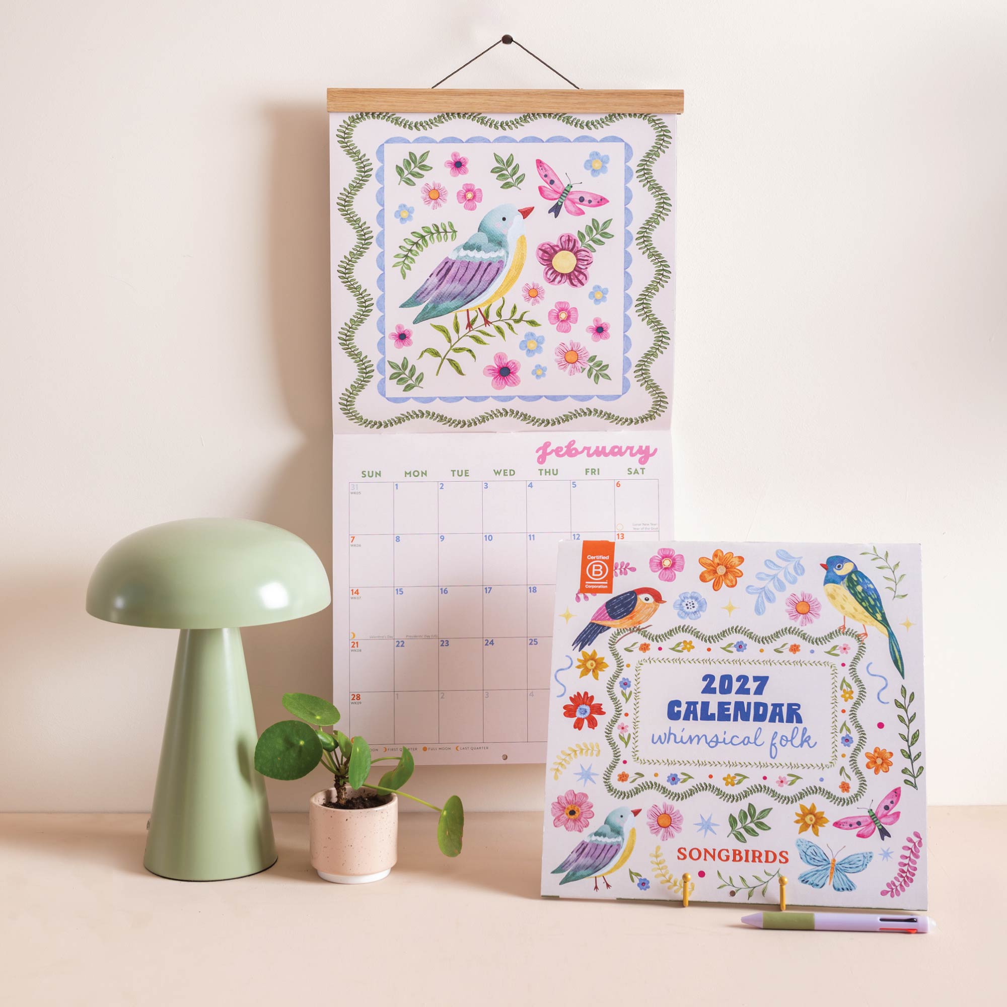 2027 wall calendar with whimsical folk-style songbird illustrations hanging on wall