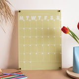 Matcha coloured Acrylic Weekly planner with days of the week in a month layout on a desk with stationery items and a vase.