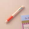 Orange multiclick erasable pen on a beige surface with a striped object in the background.