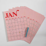 Spread of all 12 monthly pages from the pink and red A3 wall planner laid out on a surface