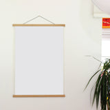 Blank white poster on a wooden frame against a light wall with a plant in the corner.