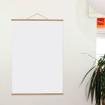 White frame with wooden border on a white wall with a plant in the corner.