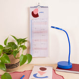 A spiral-bound April couples calendar with abstract color blocks hangs on a wall above a desk.