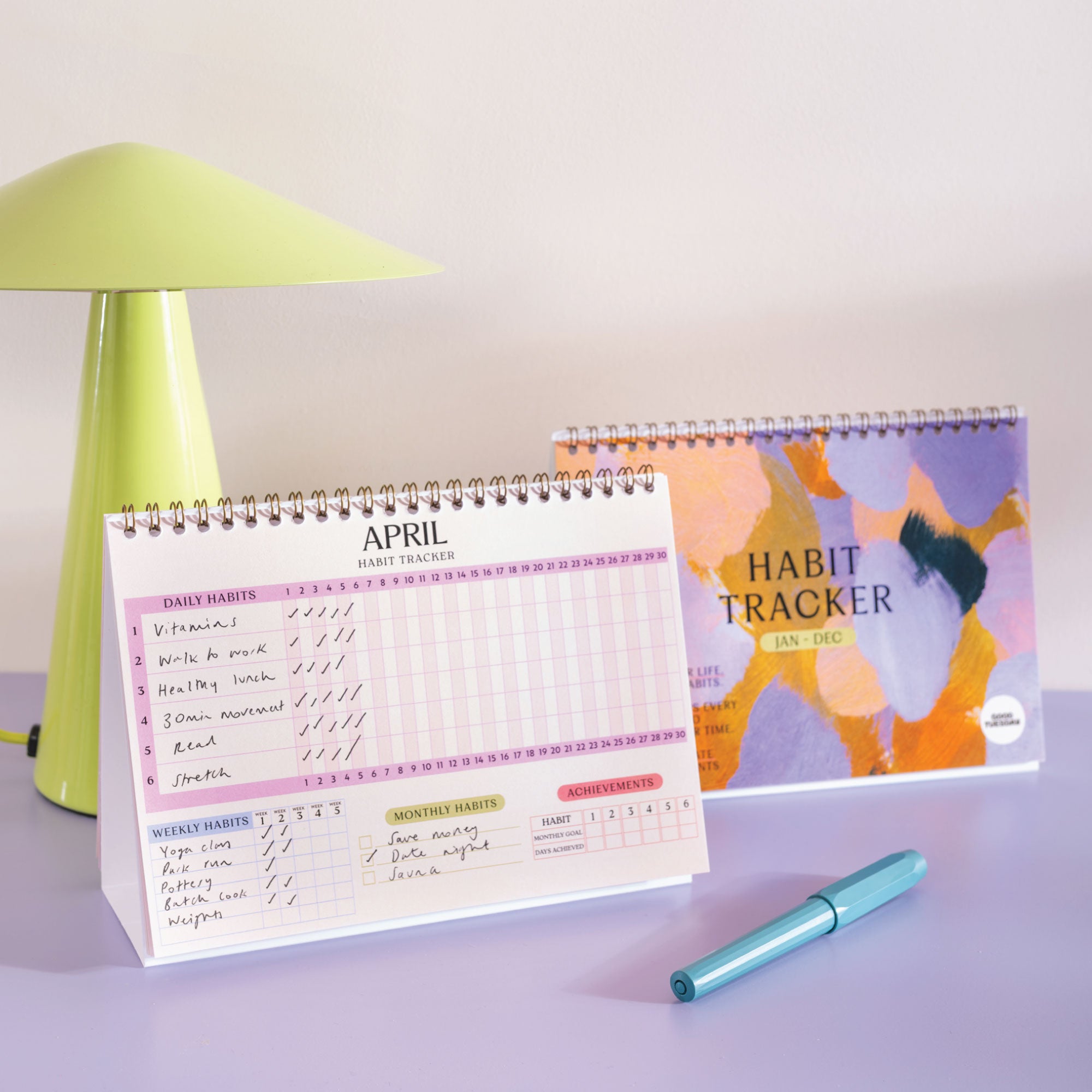 Habit tracker calendar with a pen on a light surface, next to a green lamp.
