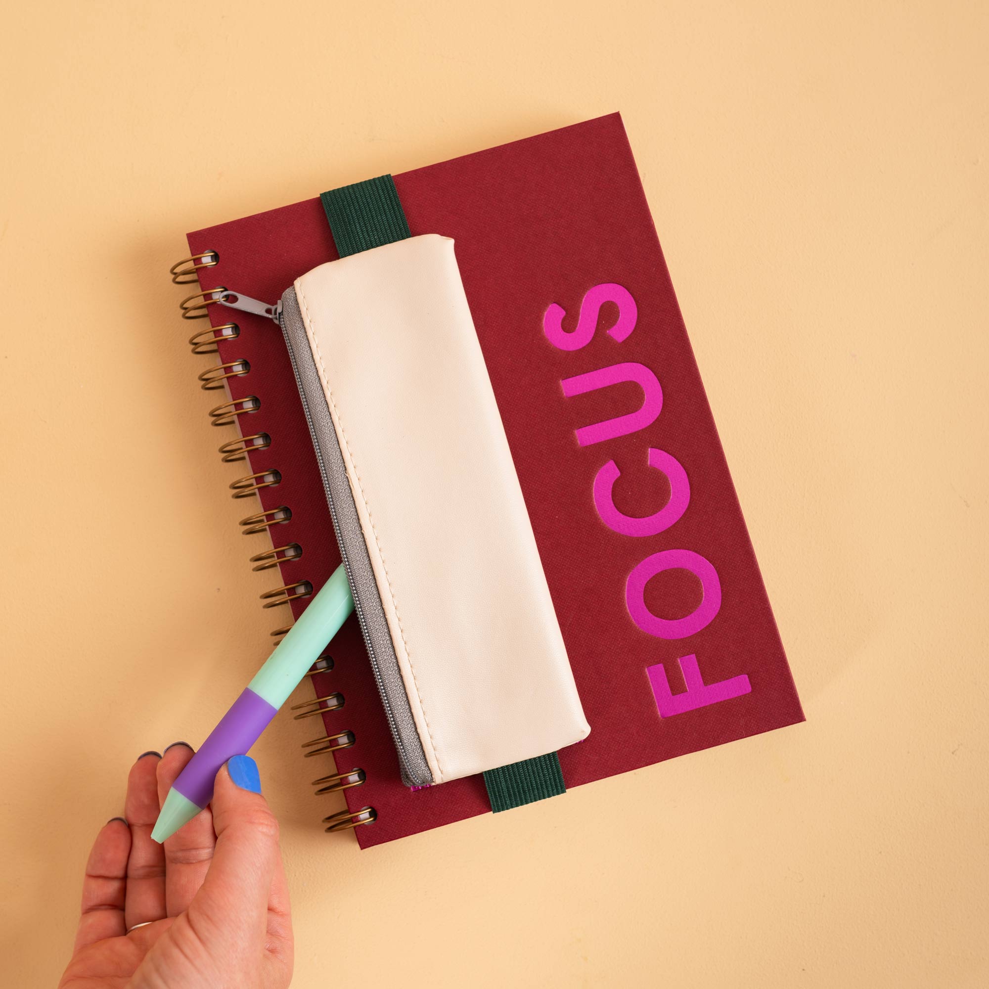 Elastic band stretches around a standard notebook to hold the Cream pencil pouch in place