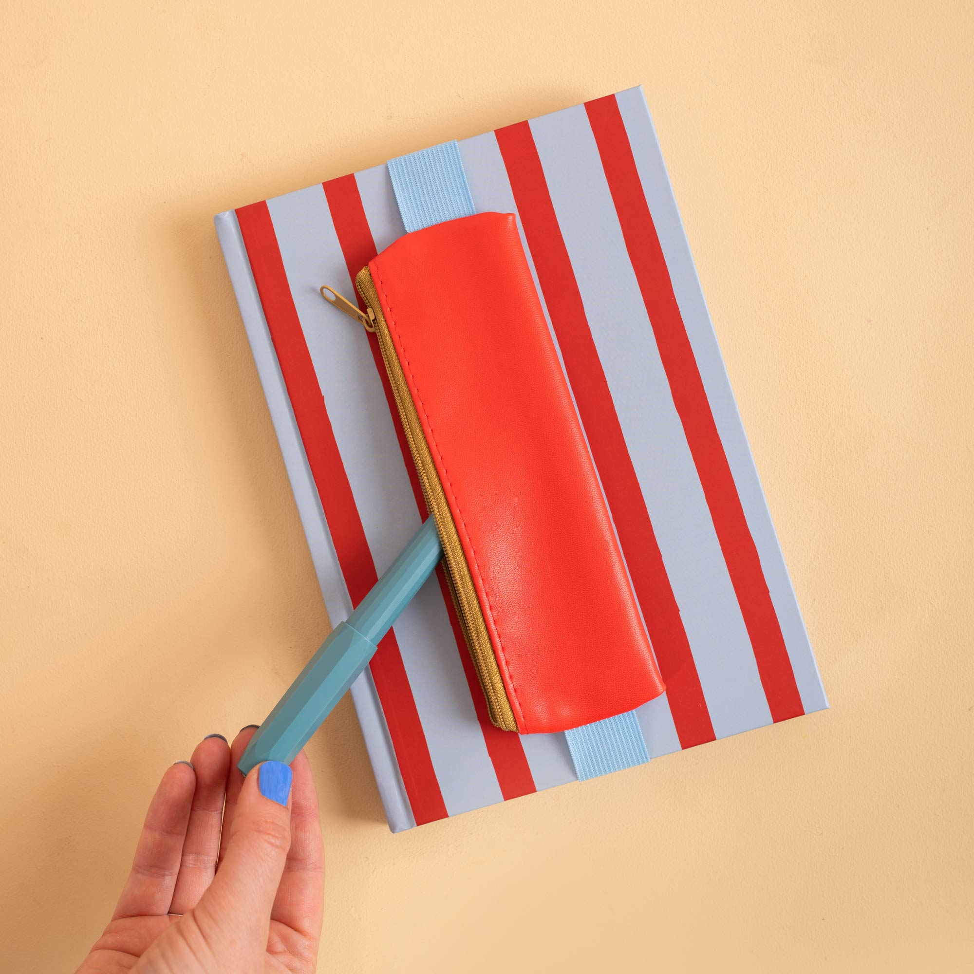 Elastic band stretches around a standard notebook to hold the Red pencil pouch in place
