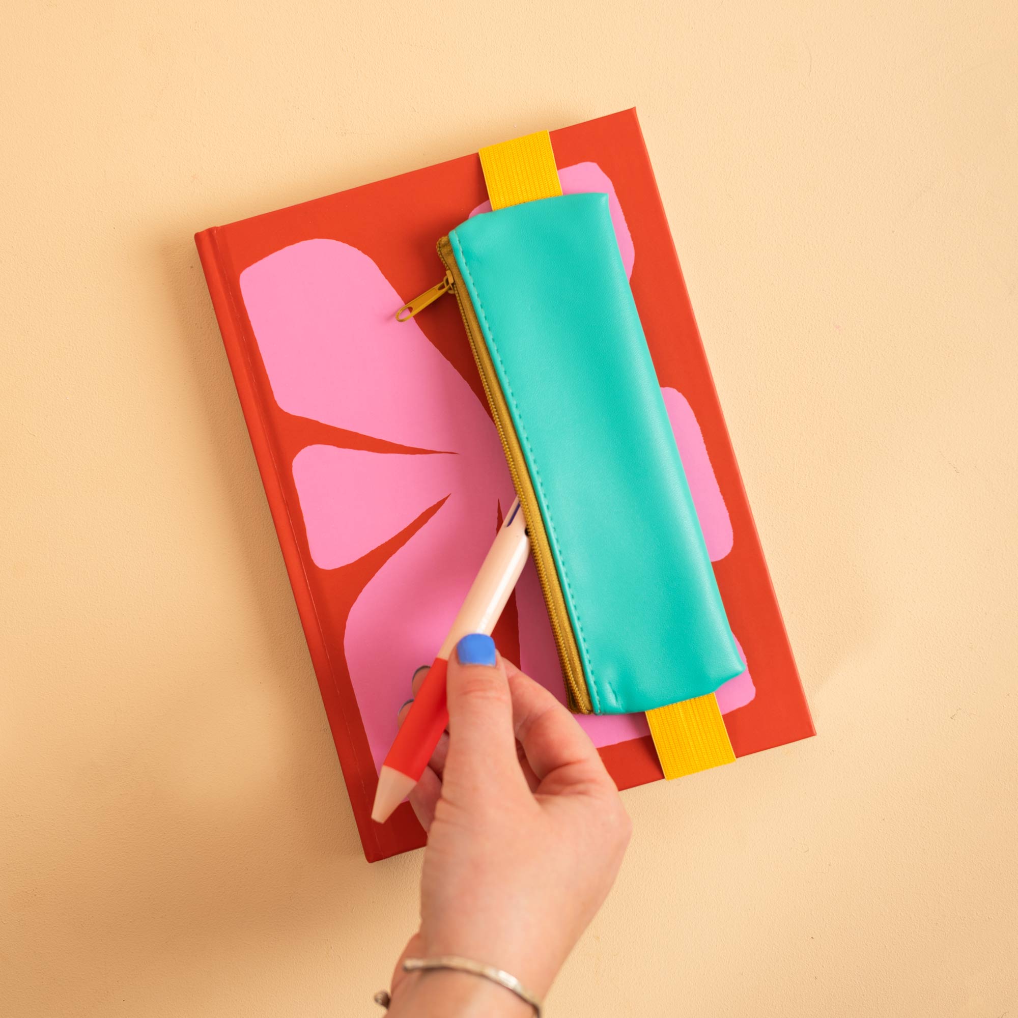 Elastic band stretches around a standard notebook to hold the Turquoise pencil pouch in place