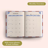 Open planner showing month-to-view January 2027 with moon phases and bank holidays on a pink background.