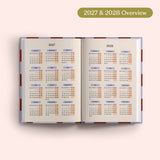 Open planner showing 2027 and 2028 yearly overview on a pink background.