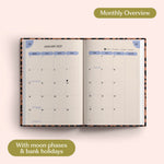 Open planner showing month-to-view January 2027 with moon phases and bank holidays on a pink background.