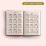 Open planner showing 2027 and 2028 yearly overview on a pink background.