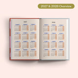 Open planner showing 2027 and 2028 yearly overview on a pink background.
