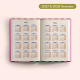 Open planner showing 2027 and 2028 yearly overview on a pink background.