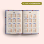 Open planner showing 2027 and 2028 yearly overview on a pink background.
