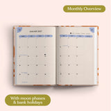 Open planner showing month-to-view January 2027 with moon phases and bank holidays on a pink background.