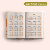 Open planner showing 2027 and 2028 yearly overview on a pink background.