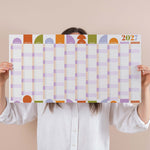 Person holding a compact pastel 2027 wall planner with colourful squares on a beige background