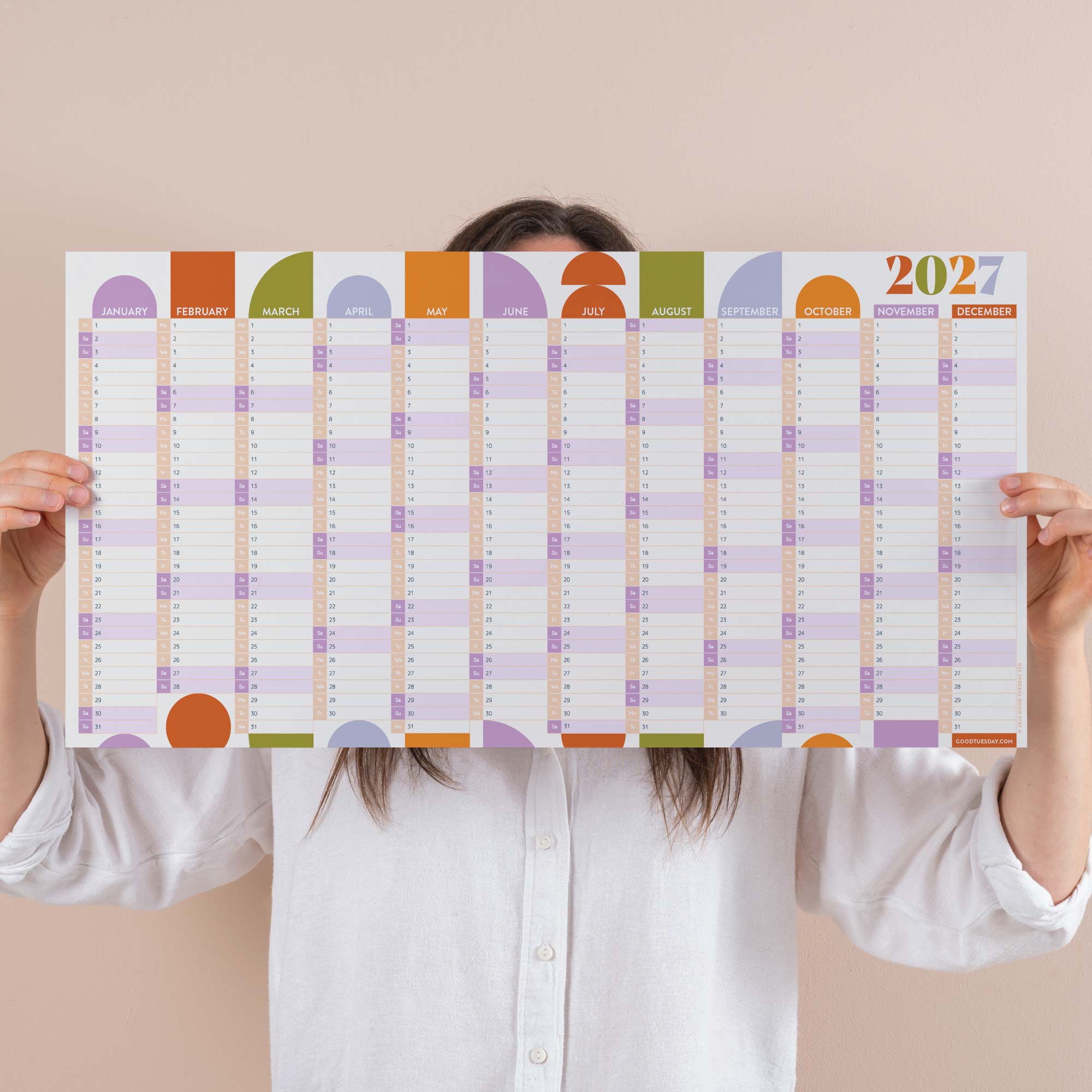 Person holding a compact pastel 2027 wall planner with colourful squares on a beige background