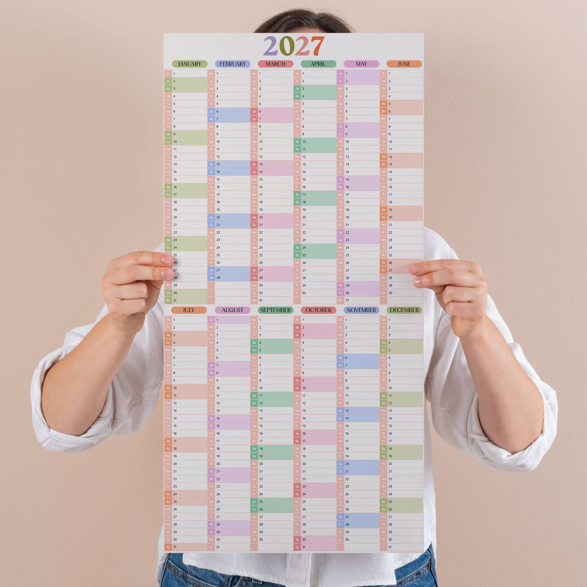 Person holding a compact pastel 2027 wall planner with colourful squares on a beige background