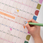 Hand with a green marker writing on a colorful calendar
