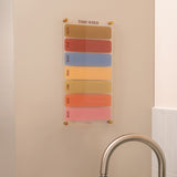 Wipeable weekly acrylic planner with spacious daily layout in an earthy colour palette mounted on a wall 