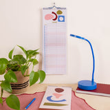 A spiral-bound June calendar page with abstract pastel shapes hangs on a wall above a desk.