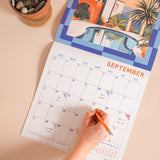 Person marking a date on a colorful September calendar with a pool and nature design.