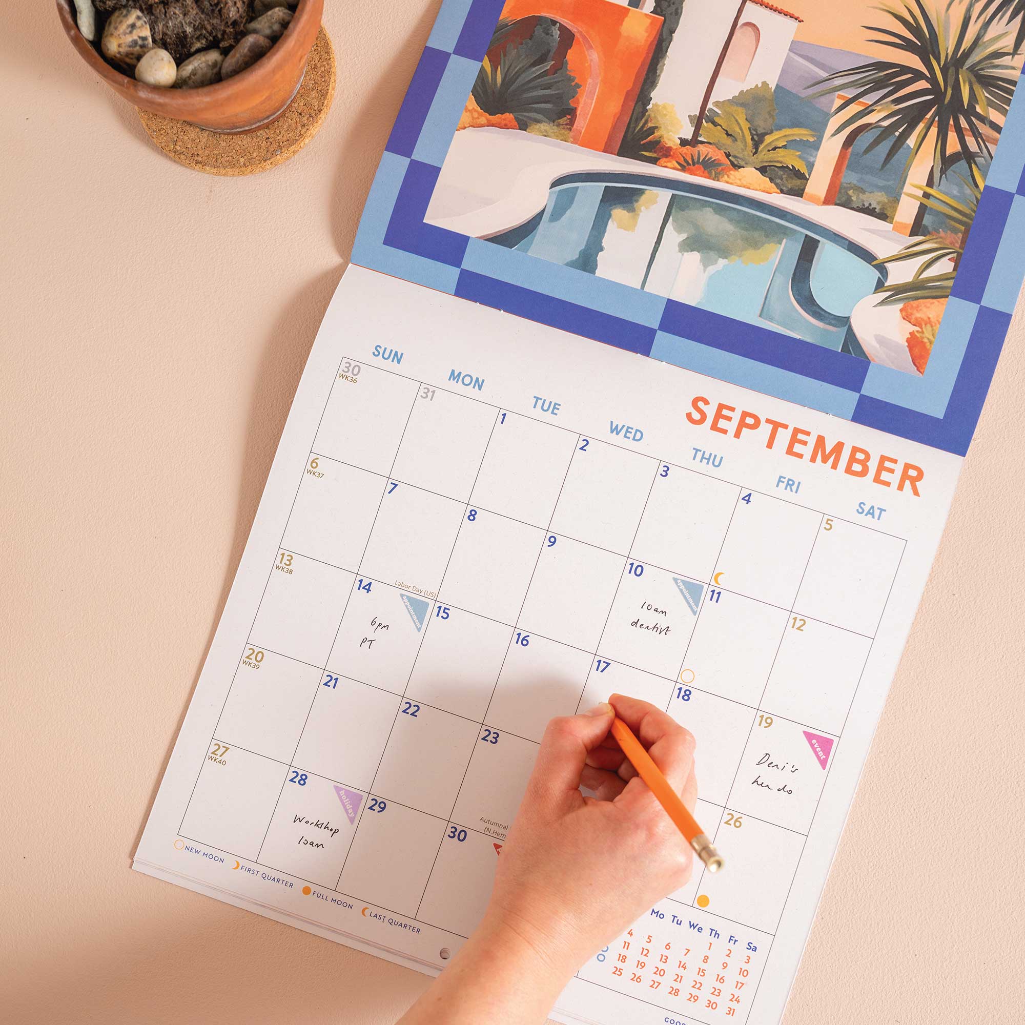 Person marking a date on a colorful September calendar with a pool and nature design.