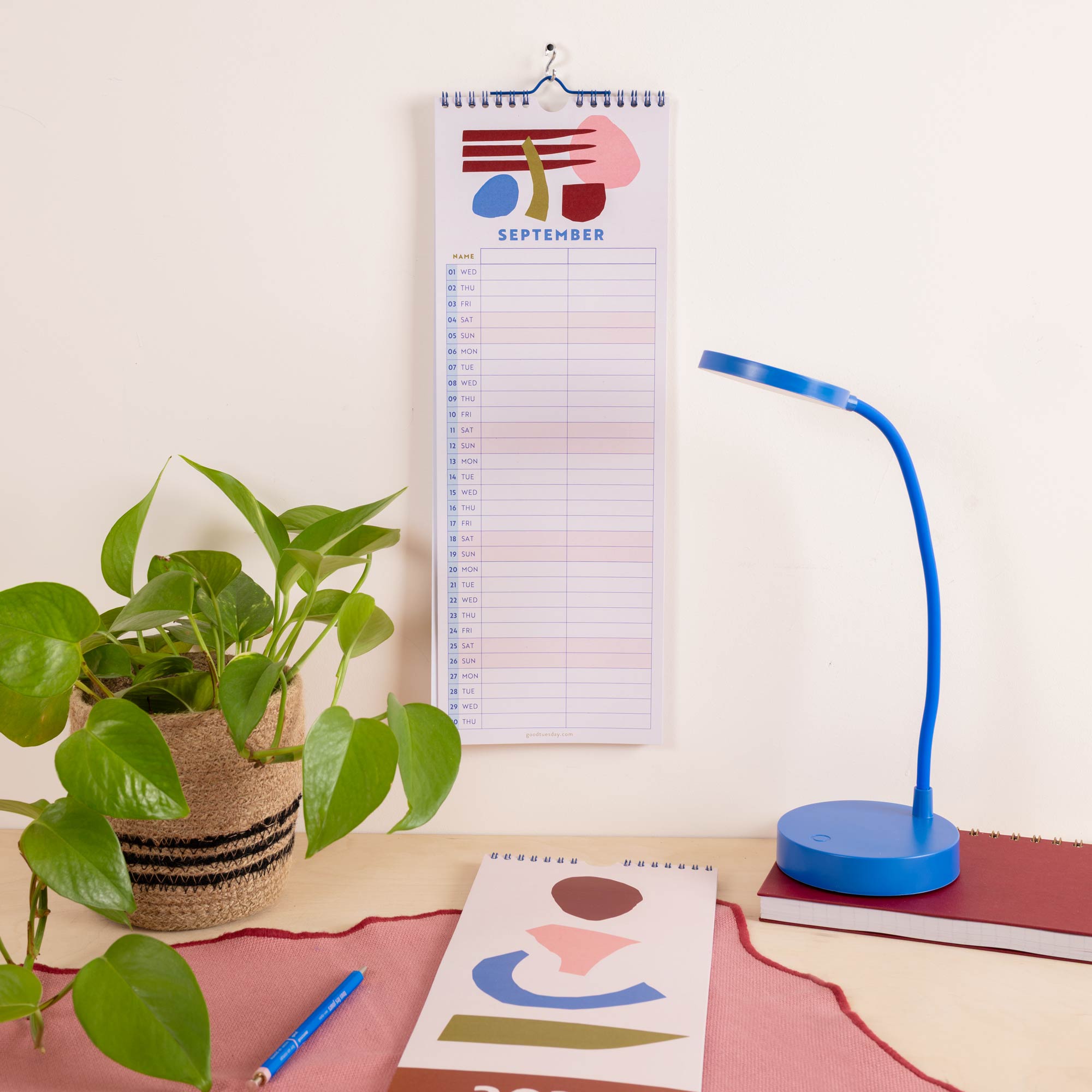 A spiral-bound September desk calendar hangs on a wall above a desk setup.