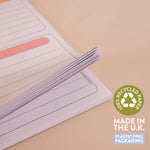 A close-up of a lined paper notepad or planner insert with a fanned stack of pages, shown on a warm beige background. A green circular badge reads '100% Recycled Paper' and text at the bottom says 'Made in the U.