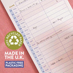 A close-up of a lined weekly planner page with handwritten notes, placed on a pink textured surface. A green circular badge reads '100% Recycled Paper' with additional text 'Made in the UK.