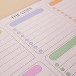 A close-up of a pastel planner notepad page titled 'THE LISTS' with lined sections and colored highlight blocks in lavender, green, pink, and orange.