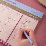 Person writing on a planner with a pink background