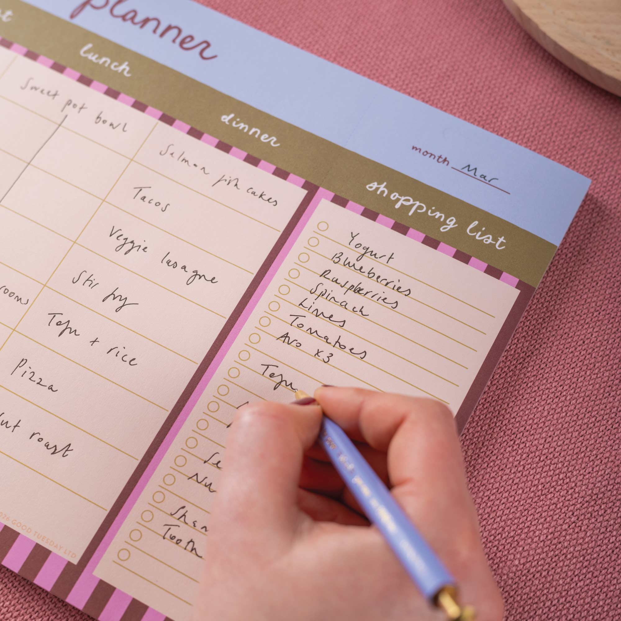 Person writing on a planner with a pink background