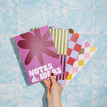 Colorful notebooks with geometric patterns held against a blue tiled wall.