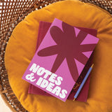 Notebook with a purple and pink cover and 'NOTES & IDEAS' text on a yellow cushion.