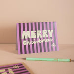 Striped 'Merry Christmas' card with a pen on a beige background