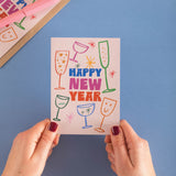 Hand holding a 'Happy New Year' card with colorful drink illustrations on a blue background
