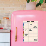 Pink refrigerator with a couples fridge magnet set against a kitchen background.