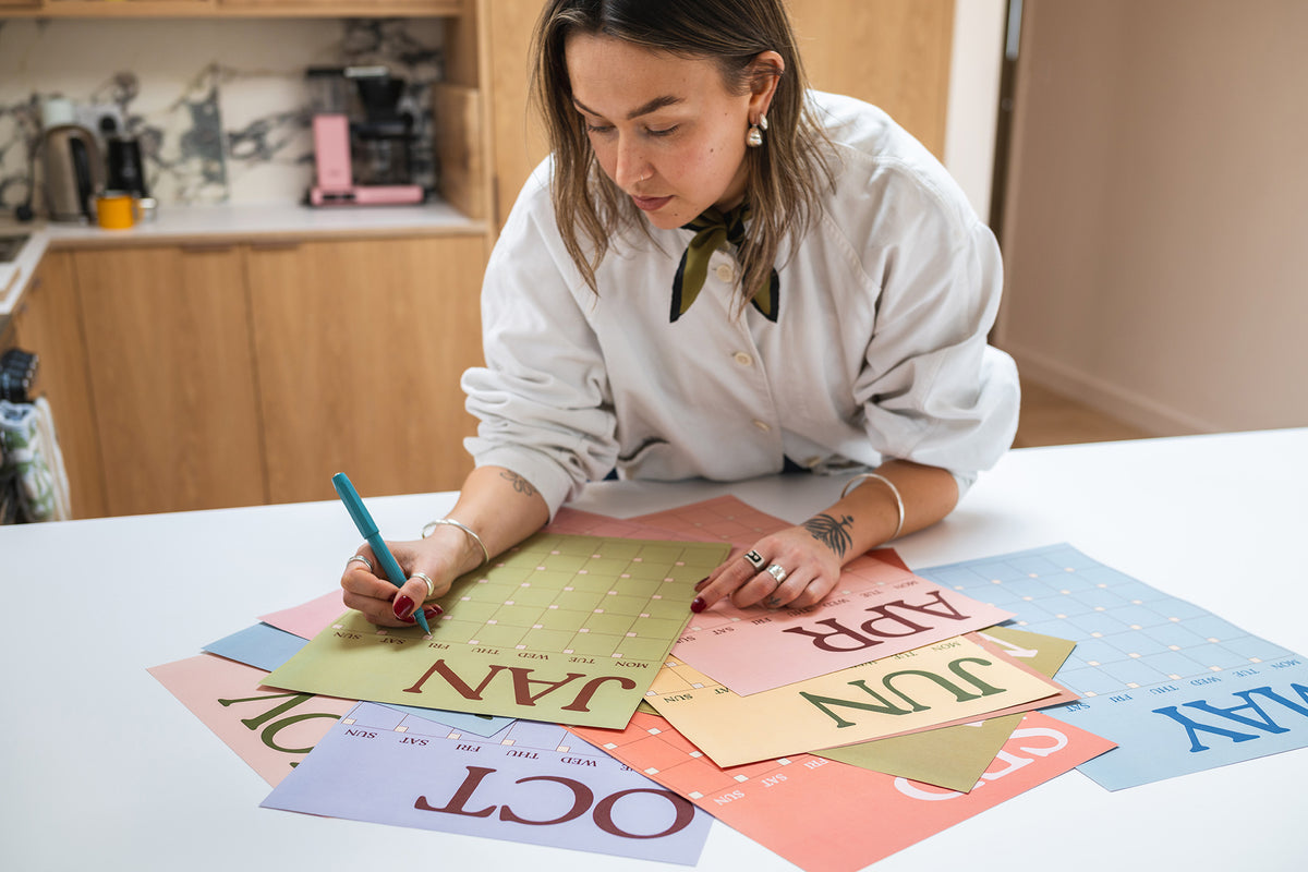 Woman planning the year on colorful calendar sheets on a table in a kitchen.
